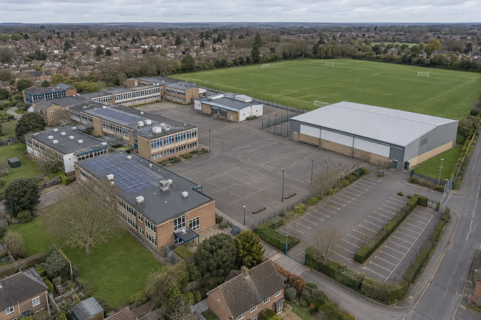 Aerial view of a school site with teaching blocks of several different ages, a sports hall and a playing field, solar arrays on two of the flat roofs