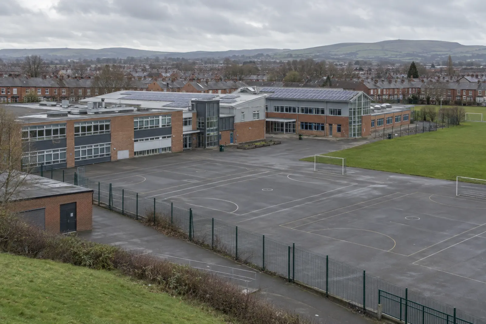 A school on the edge of a Greater Manchester town, solar arrays on its roofs and low Pennine hills beyond