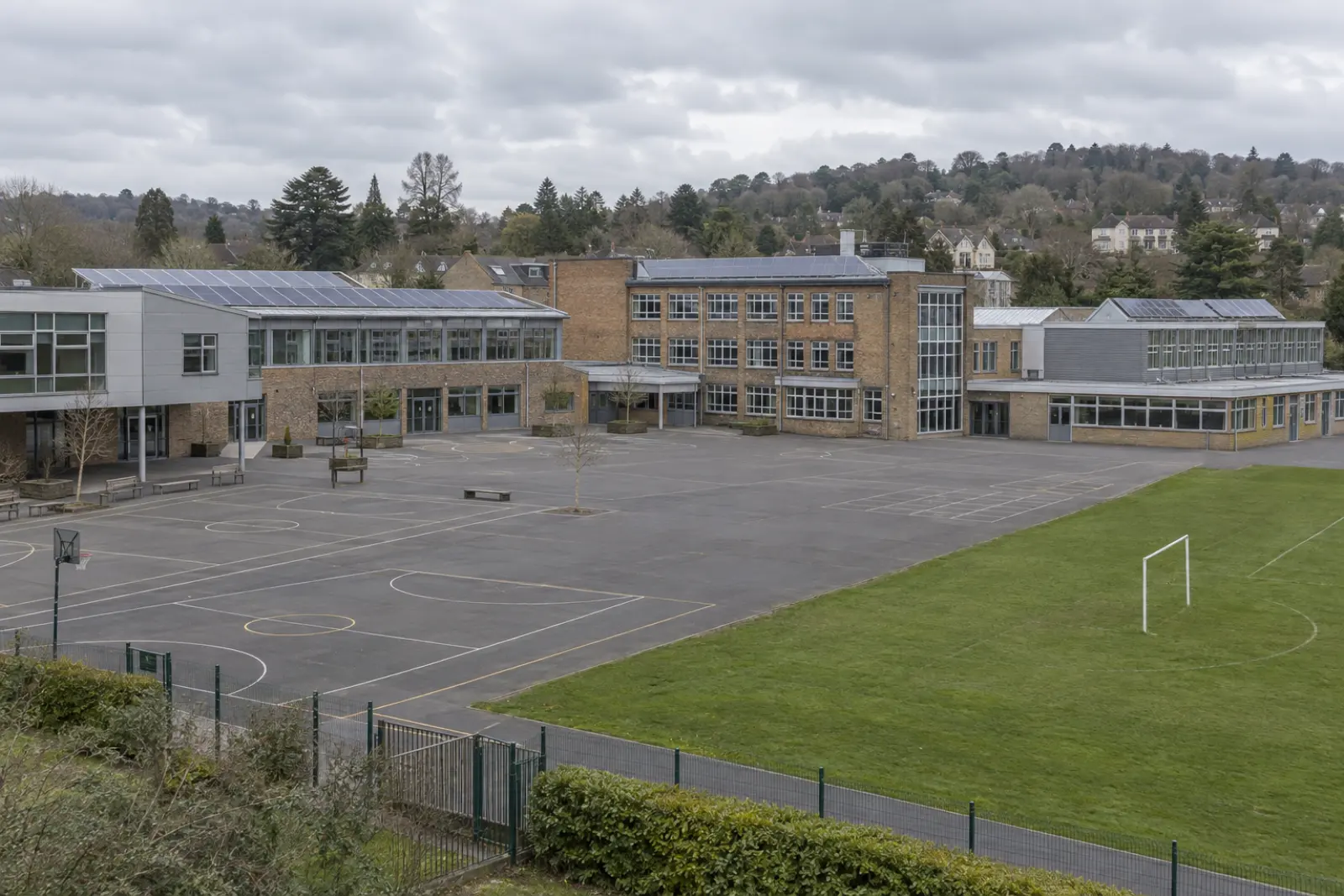 A school on the edge of a Home Counties town, solar arrays on its roofs and wooded low hills beyond
